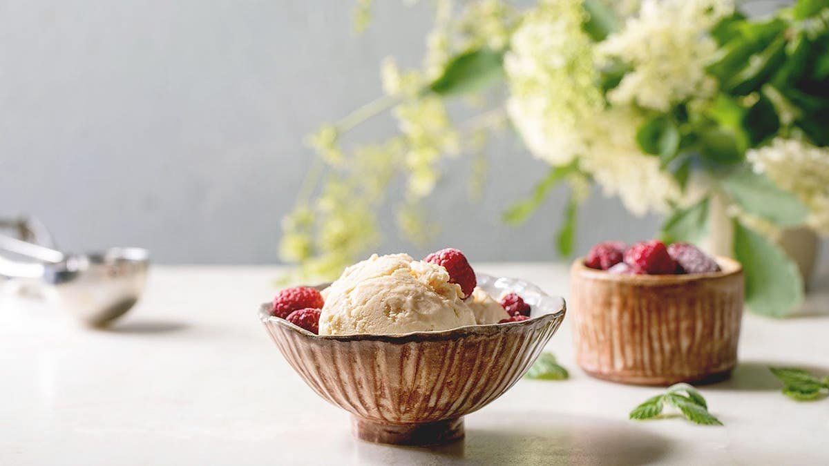 Homemade caramel vanilla ice cream with frozen raspberries in a ceramic bowl on a white marble table.