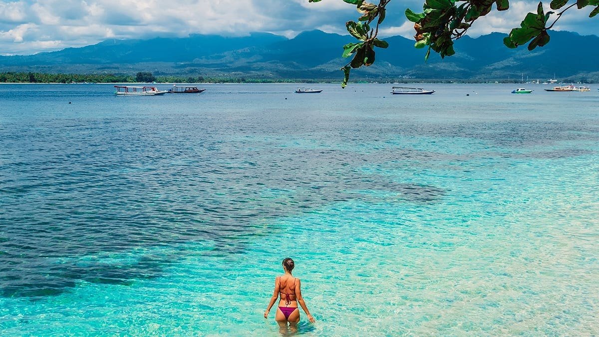 Woman in bikini relaxes in blue ocean water on a tropical island.